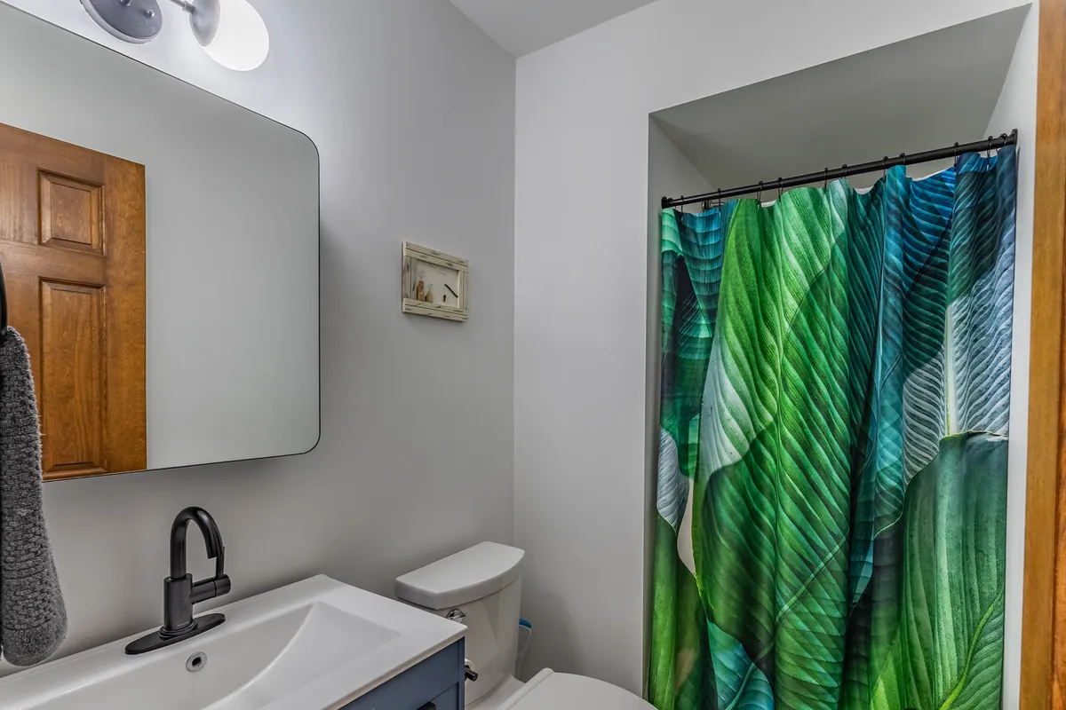 A tranquil bathroom with a colorful shower curtain, modern sink and faucet, large mirror, and wooden accents. The space exudes a sense of calm and is perfect for both morning routines and evening relaxation.