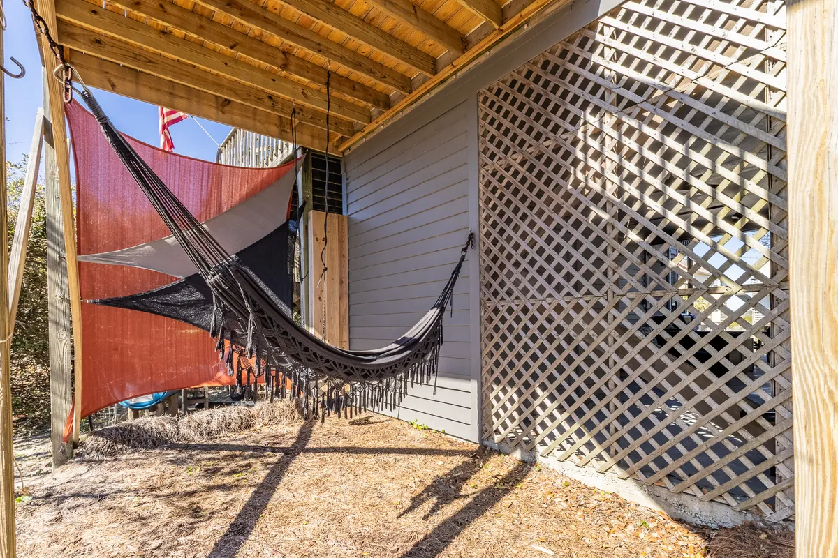 A cozy outdoor hammock is strung beneath colorful fabric shades on a shaded deck, with a lattice wall providing privacy. The calm, inviting scene highlights a perfect spot for a midday break or quiet reflection surrounded by gentle natural light.