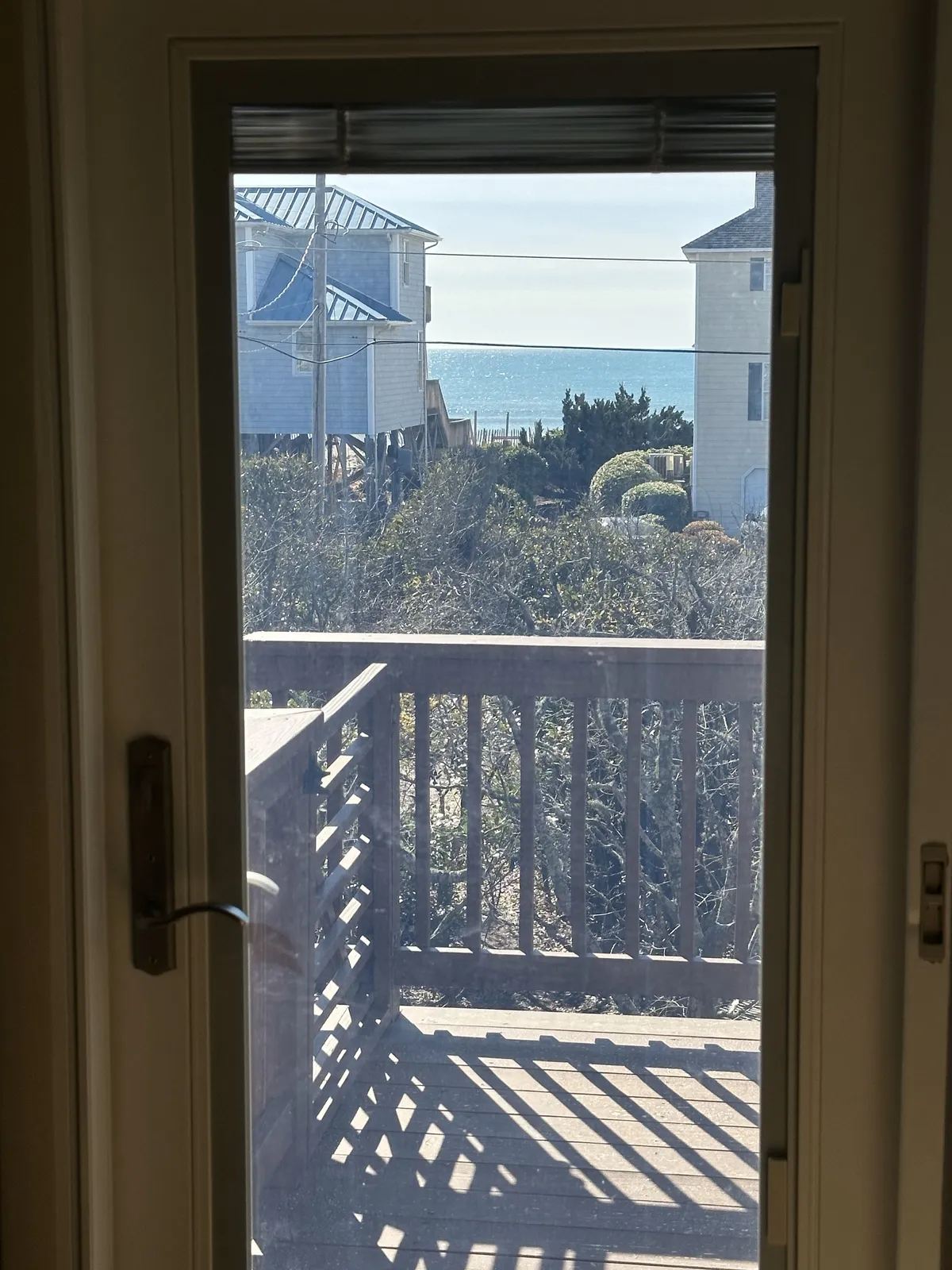 This image captures a serene ocean view from a private balcony, framed by surrounding houses. The scene shows someone relaxing and enjoying the tranquil atmosphere, possibly reading or soaking in the peaceful setting. The soft light and horizon evoke a sense of calm and inspiration.