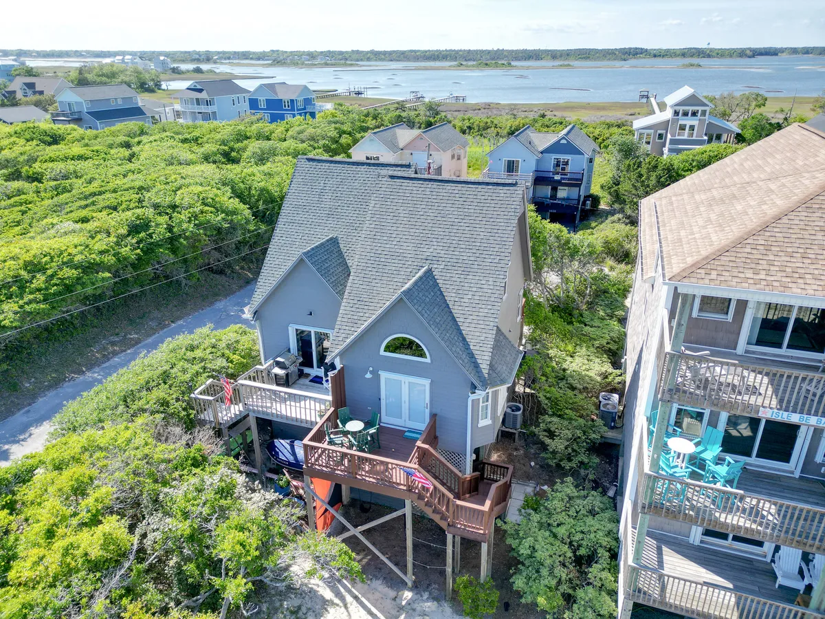 A bright, spacious deck with the house, greenery, and water views in the background. Comfortable seating invites guests to relax, dine, or savor sunset and sunrise vistas over the water.