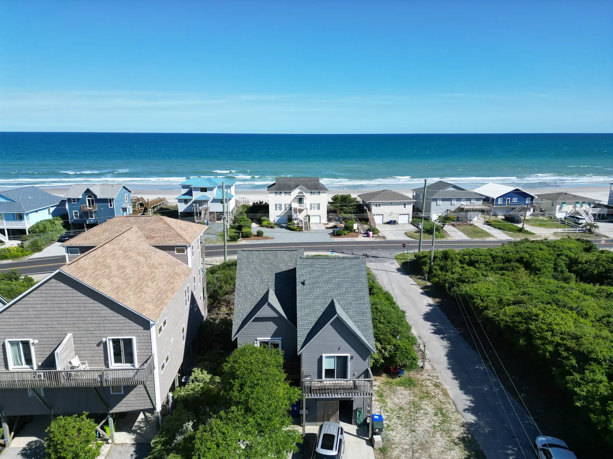 This image features a sweeping ocean view with beachfront houses and lush green foliage lining a roadway. The scene captures the tranquility of Surf City and hints at the proximity to both beach and local attractions, with the soft lighting suggesting either sunrise or sunset.