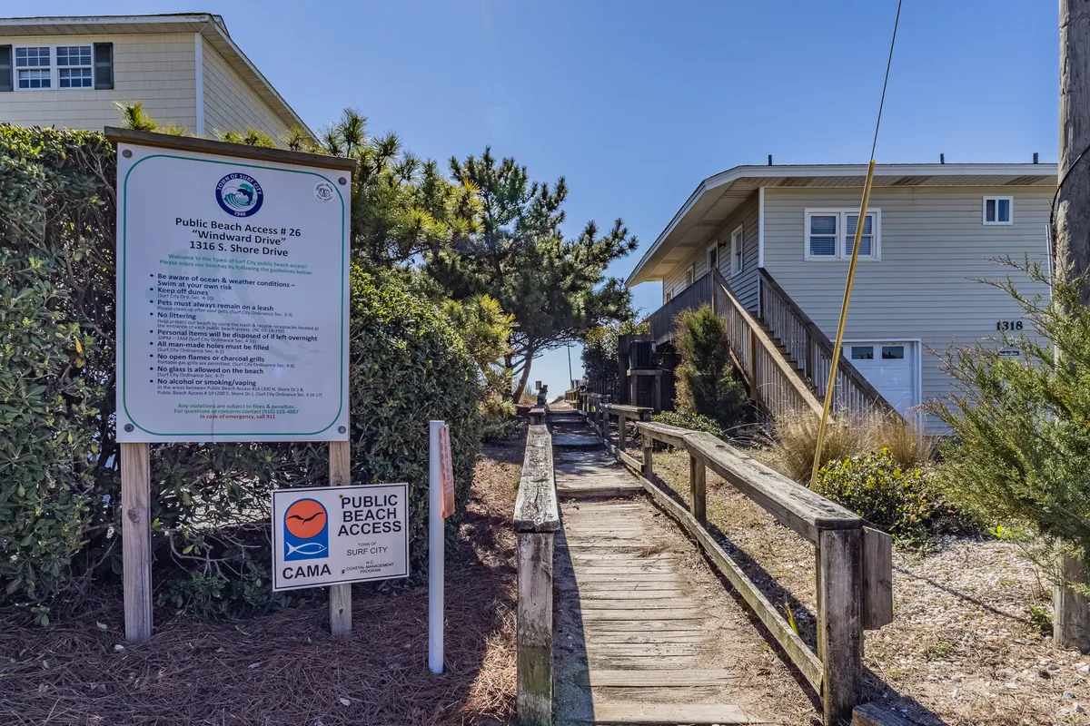 This image features the 'Public Beach Access' sign, a wooden walkway, and lush surrounding greenery. It conveys the transition from the neighborhood directly onto the beach, capturing the ease and invitation of stepping from home to sand.