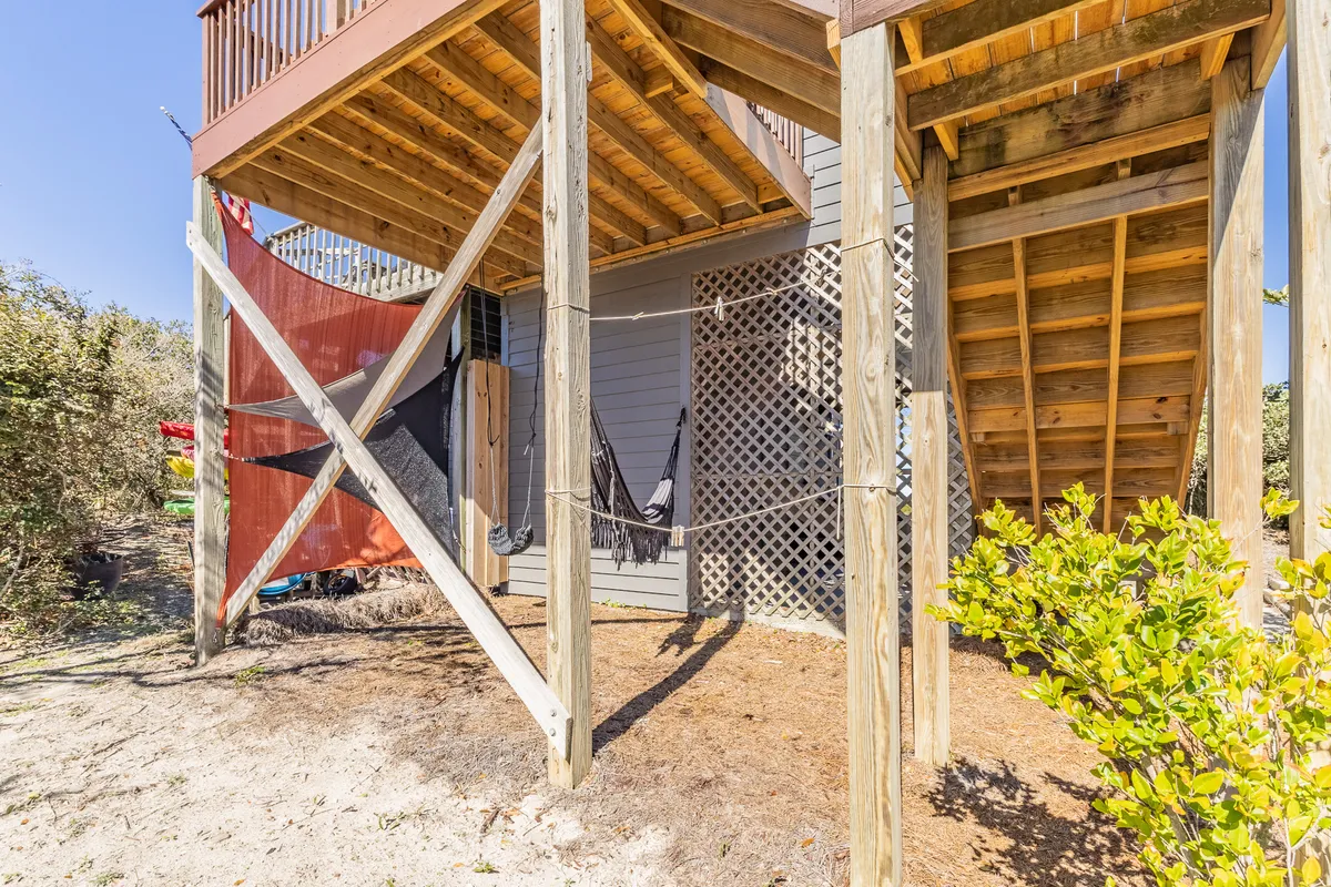 A hammock is strung between sturdy wooden posts on a sun-dappled deck, with lattice work providing privacy and a cozy ambiance. The scene evokes feelings of leisure, perfect for napping or reading as gentle sea breezes pass through.